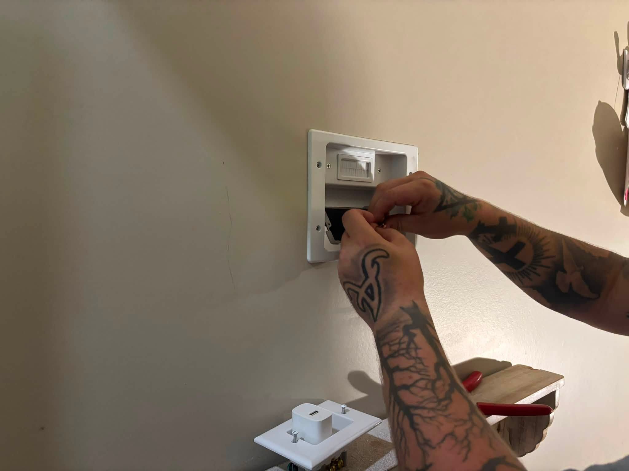 Hands installing a recessed in-wall power plate for a TV mount